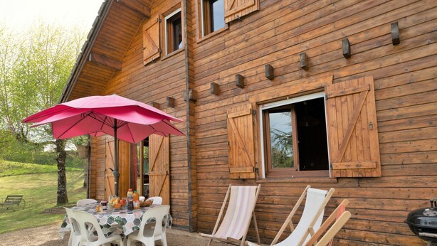 Una baita di legno con patio, dotata di tavolo, sedie e barbecue.