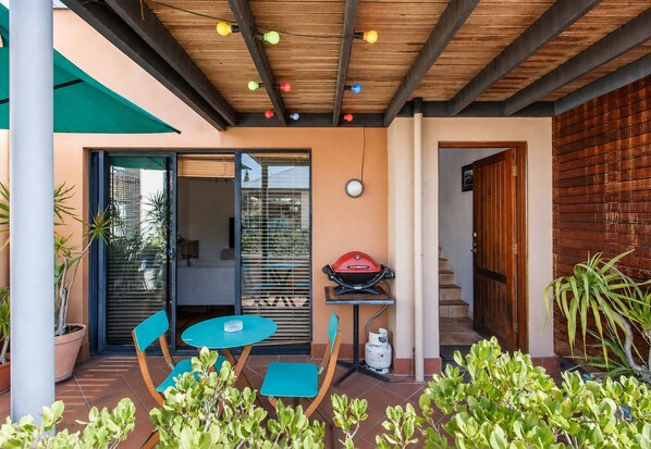 An outdoor patio with a table and chairs, a barbecue grill, and potted plants.