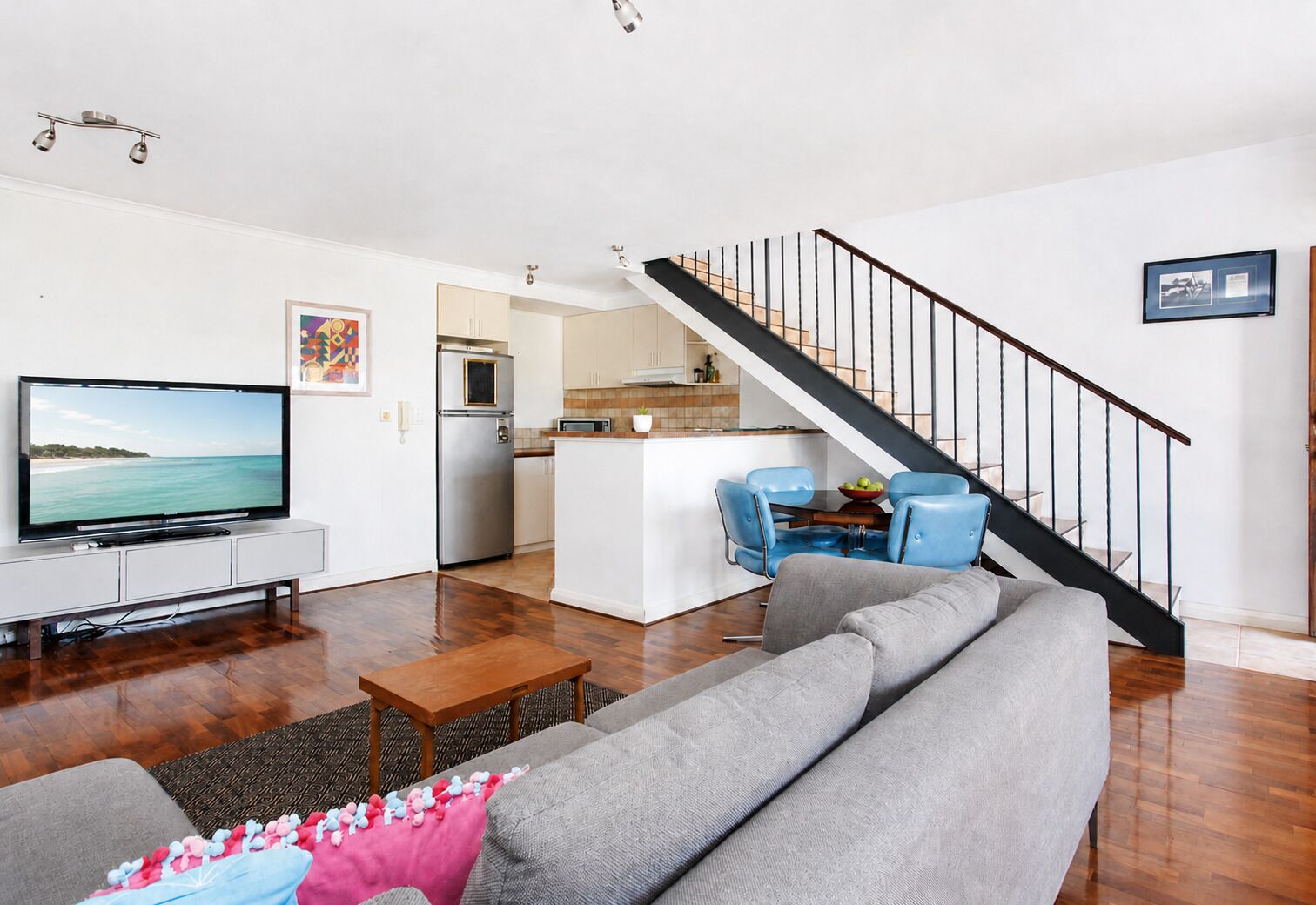 A living room with a television, sofa, coffee table, and a staircase leading to a kitchen.