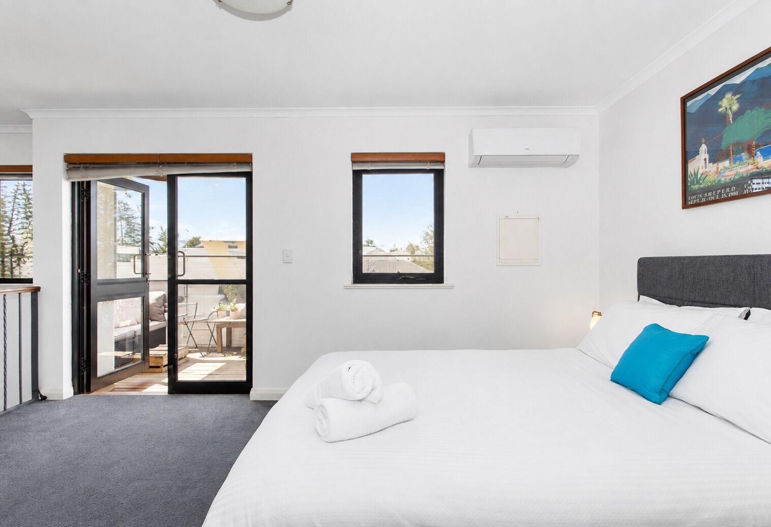 A hotel room with a bed, a window, a door leading to a balcony, and a painting on the wall.