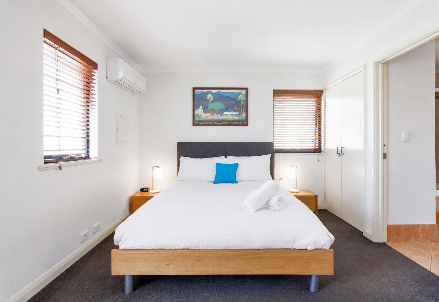 A hotel room with a bed, two bedside tables, a nightstand, a painting, and a door.