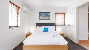 A hotel room with a bed, two bedside tables, a nightstand, a painting, and a door.