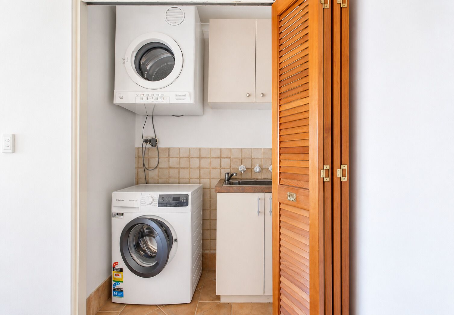 A compact laundry room with a front-loading washing machine, a small cabinet, and a wooden door.