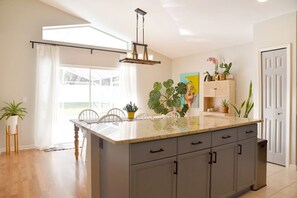 A modern kitchen with a large island, wooden cabinets, and a hanging light fixture. - SF Artisan`s Retreat - Poolside Paradise near Disney (Clermont)