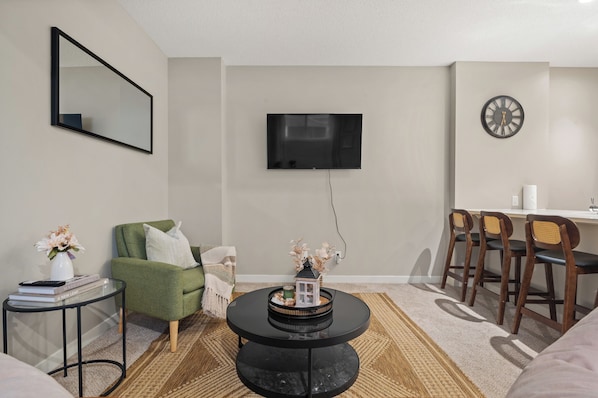 A modern living room with a flat-screen TV, a green armchair, a small side table with books, and a decorative tray.