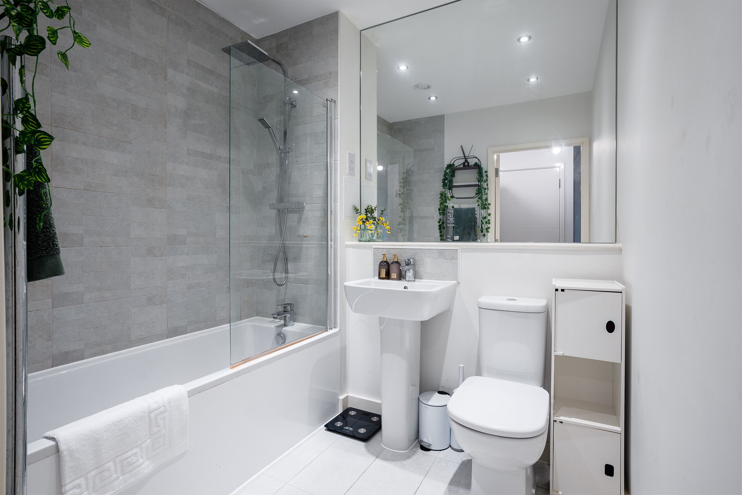 A modern bathroom with a glass-enclosed shower, a white sink, and a toilet.
