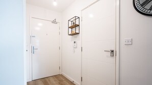 A hallway with white walls, a wooden floor, and a door with a metal handle. - Charming 1-bed Apartment in London (London)