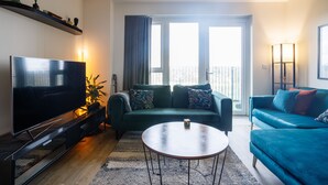 A modern living room with a flat-screen TV, two sofas, a coffee table, and a large window with curtains. - Charming 1-bed Apartment in London (London)