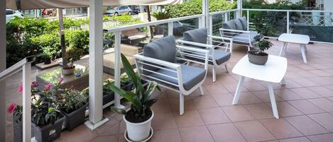 A terrace with outdoor seating, potted plants, and a view of the street.