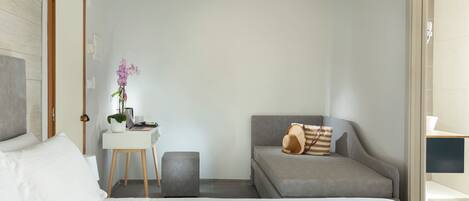 Una habitación de hotel moderna con una cama, un escritorio, un sofá gris y un taburete pequeño.