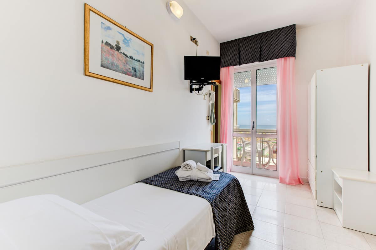 A hotel room with two beds, a television, a balcony with pink curtains, and a painting on the wall.