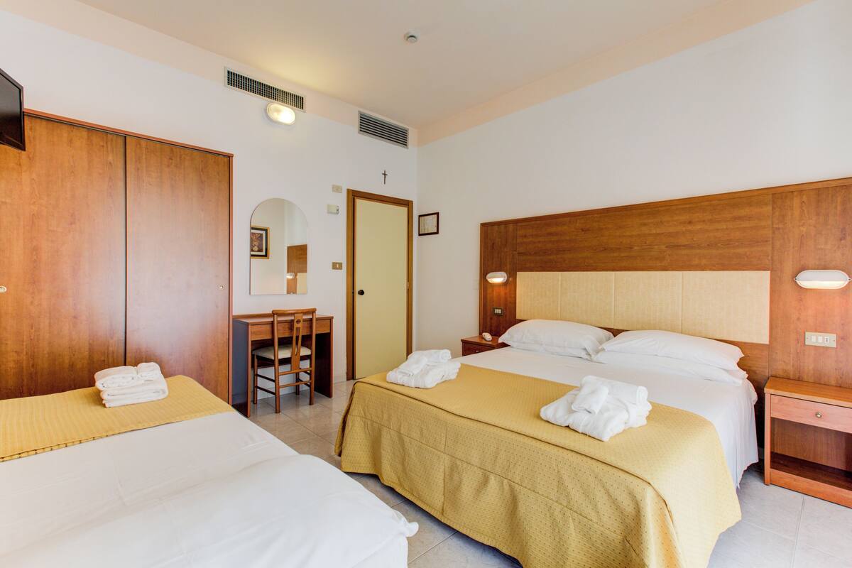A hotel room with two beds, a desk, and a mirror.