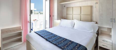 A hotel room with a bed, a nightstand, a wardrobe, and a balcony with a table and chairs.