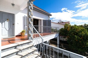 A house with a white exterior, a balcony with a metal railing, and a door with shutters.