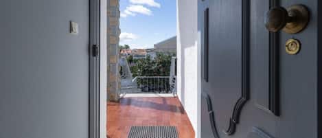 Une porte donnant sur un balcon d’où l’on peut admirer les bâtiments et un ciel dégagé.
