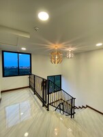 A spacious room with a large window, a staircase with black railing, and two spherical ceiling lights.