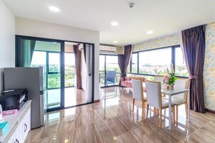 A modern hotel room with a balcony, a dining area with a table and chairs, and a TV on a cabinet.