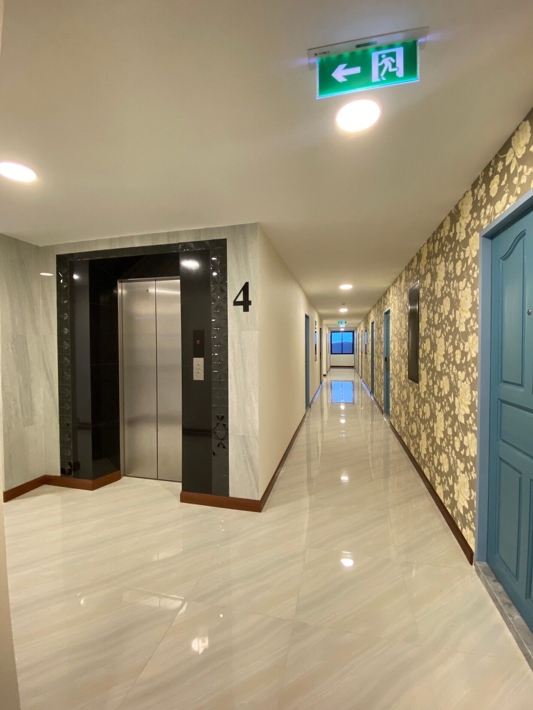 A hallway with a marble floor, a green emergency exit sign, and a blue door on the right.