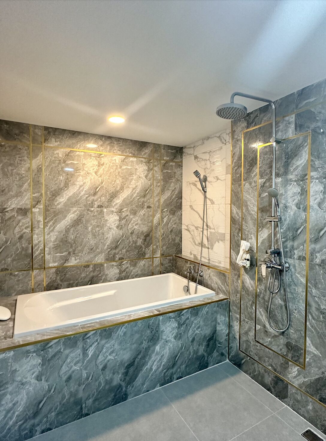 A modern bathroom with a marble wall, a freestanding bathtub, and a walk-in shower.