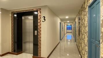 Corredor de hotel com piso lustroso, placa com o número 3, um elevador e portas azuis.