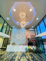A lobby with a marble floor, a reception desk, a chandelier, and large windows.