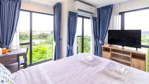 Une chambre d’hôtel avec un grand lit, une télévision, un bureau et une vue sur la verdure par les fenêtres.
