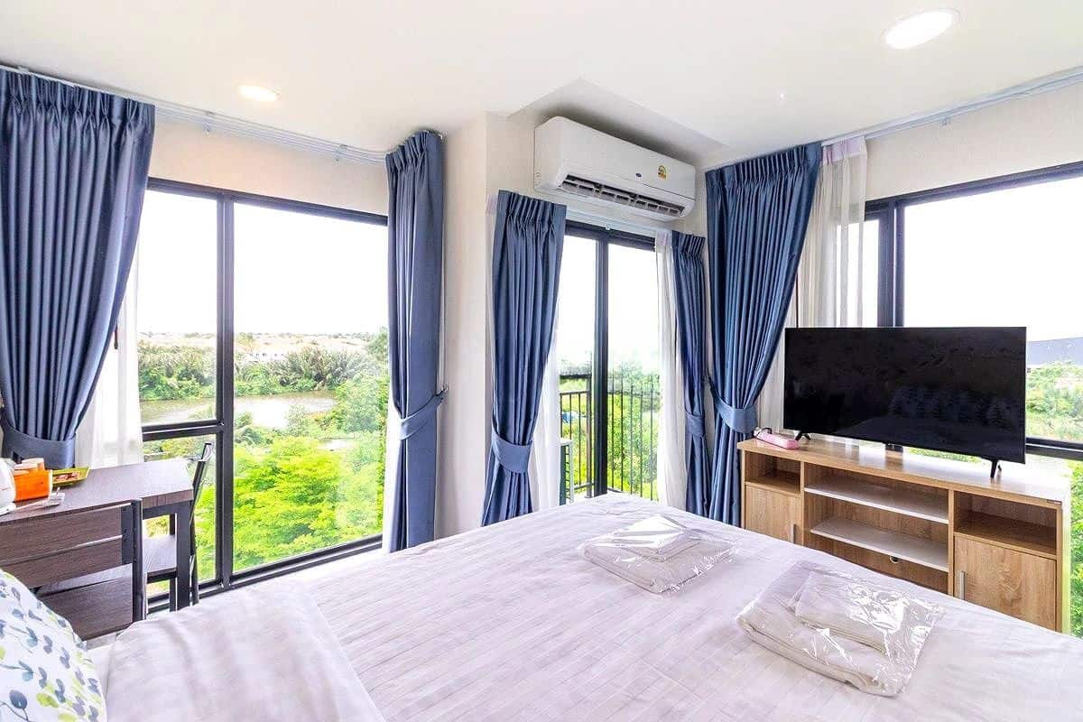 Een hotelkamer met een groot bed, een televisie, een bureau en uitzicht op groen door de ramen.