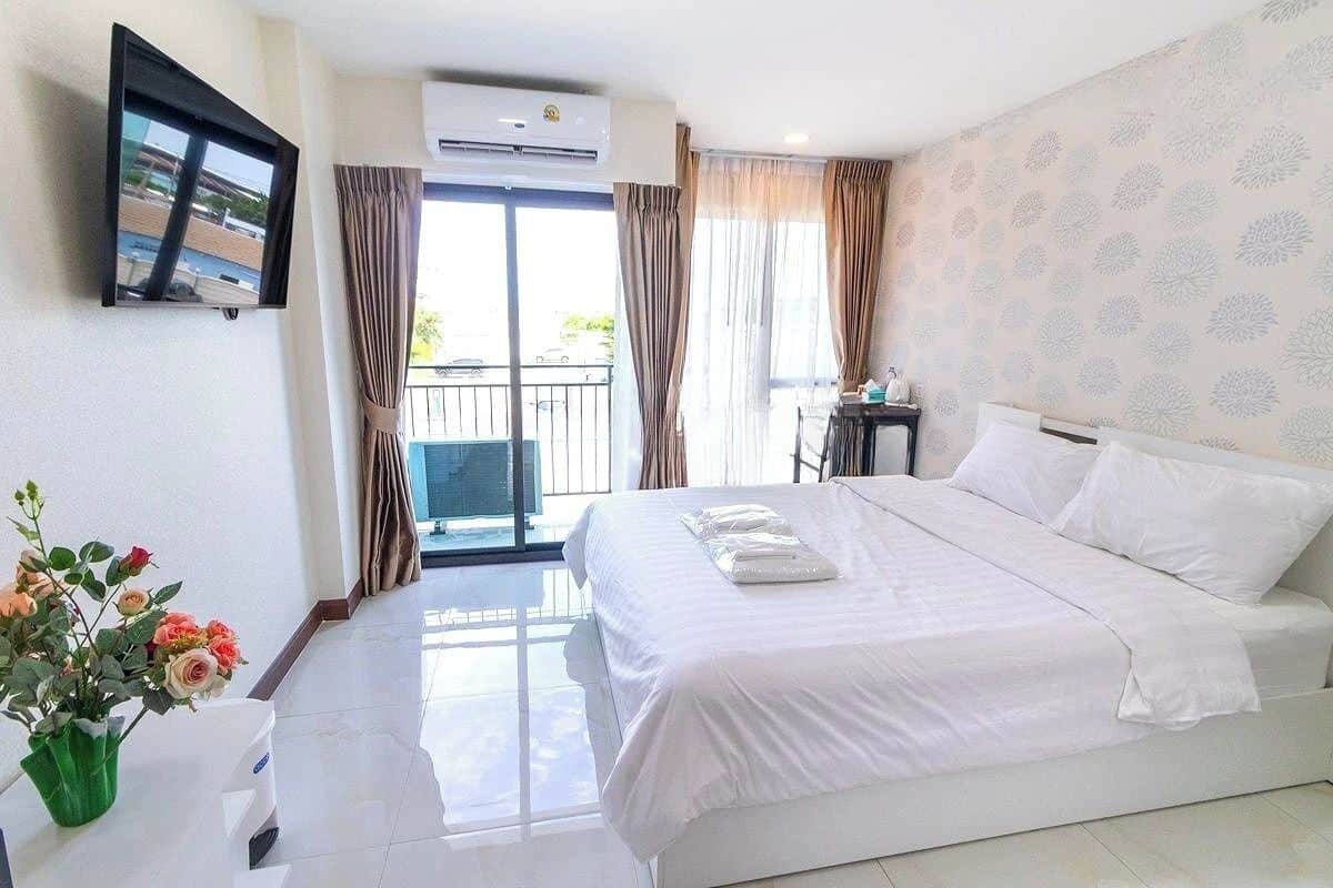 Een hotelkamer met een groot bed, een wandtelevisie, een airconditioning en een balkon met gordijnen.