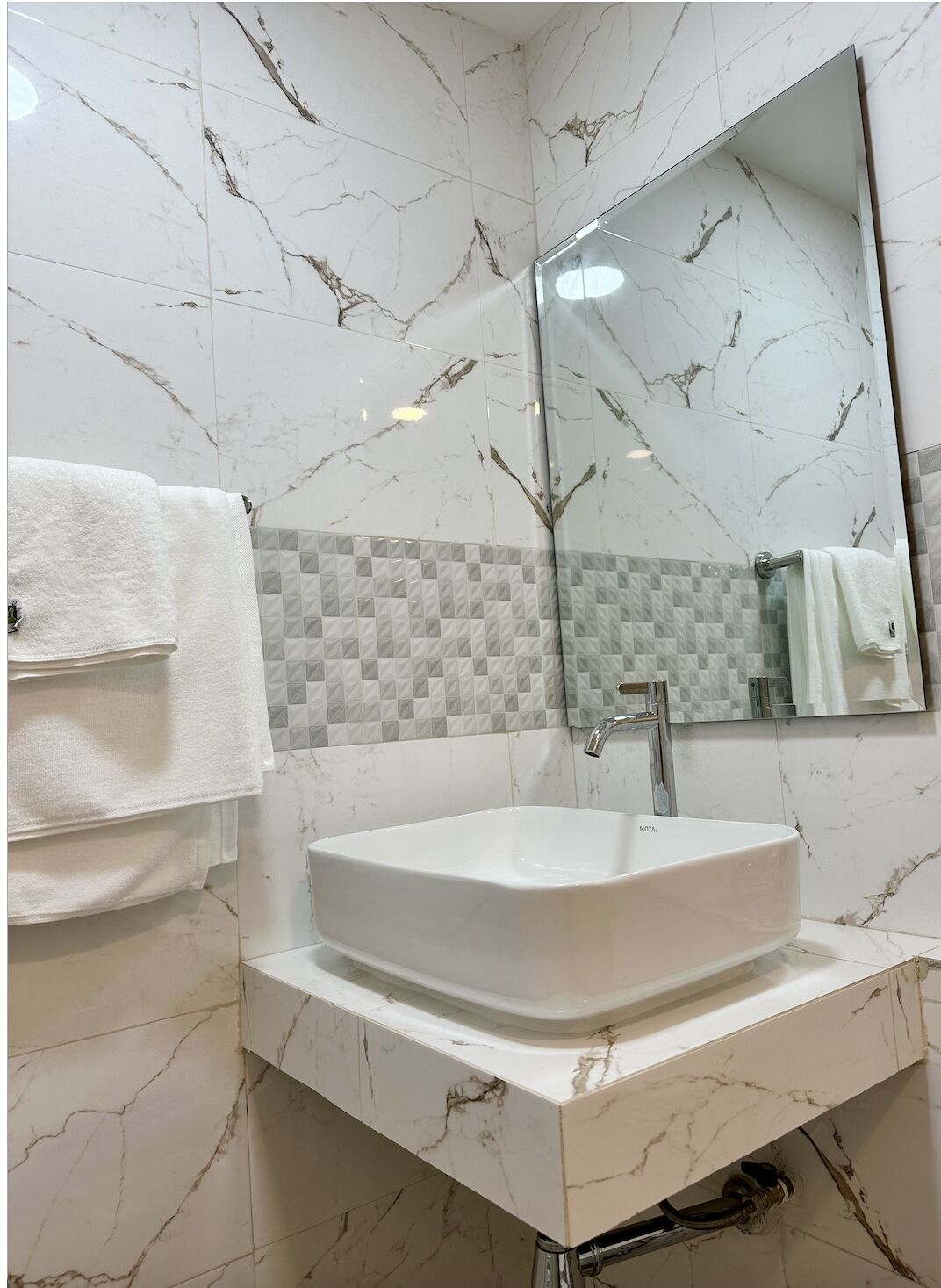 A bathroom with a white marble sink, a mirror, and a towel rack.