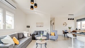 A modern living room with a grey sofa, a round coffee table, and a dining area with a white table and chairs. - Newly Built Home with Garden, 400m. to Beach (Kokkini Hani)