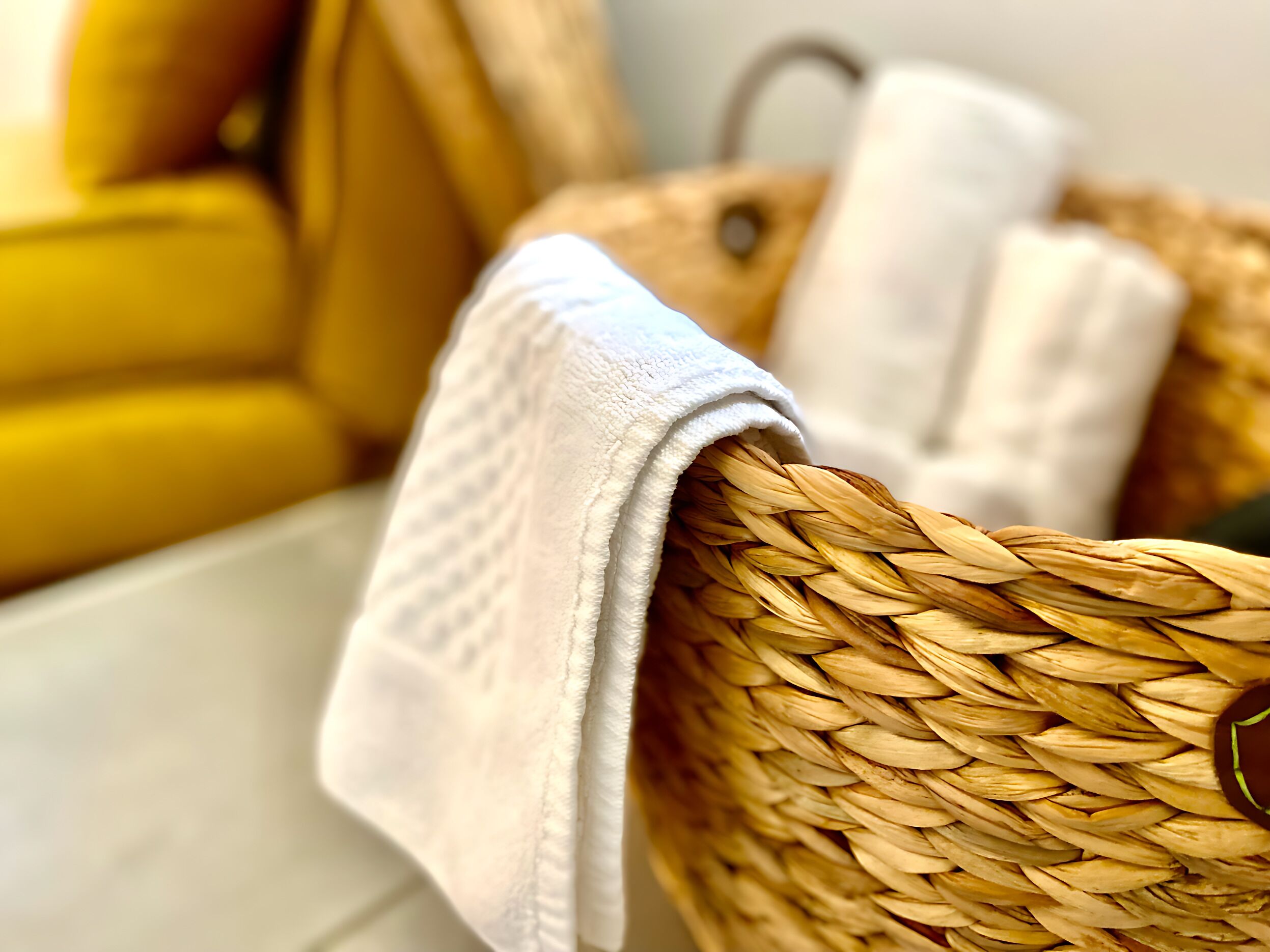 A woven basket with a white towel draped over it, placed on a wooden surface.