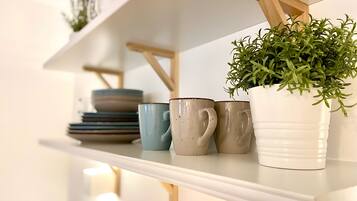 Een plank met keramische mokken, een witte pot met een groene plant en gestapelde borden.