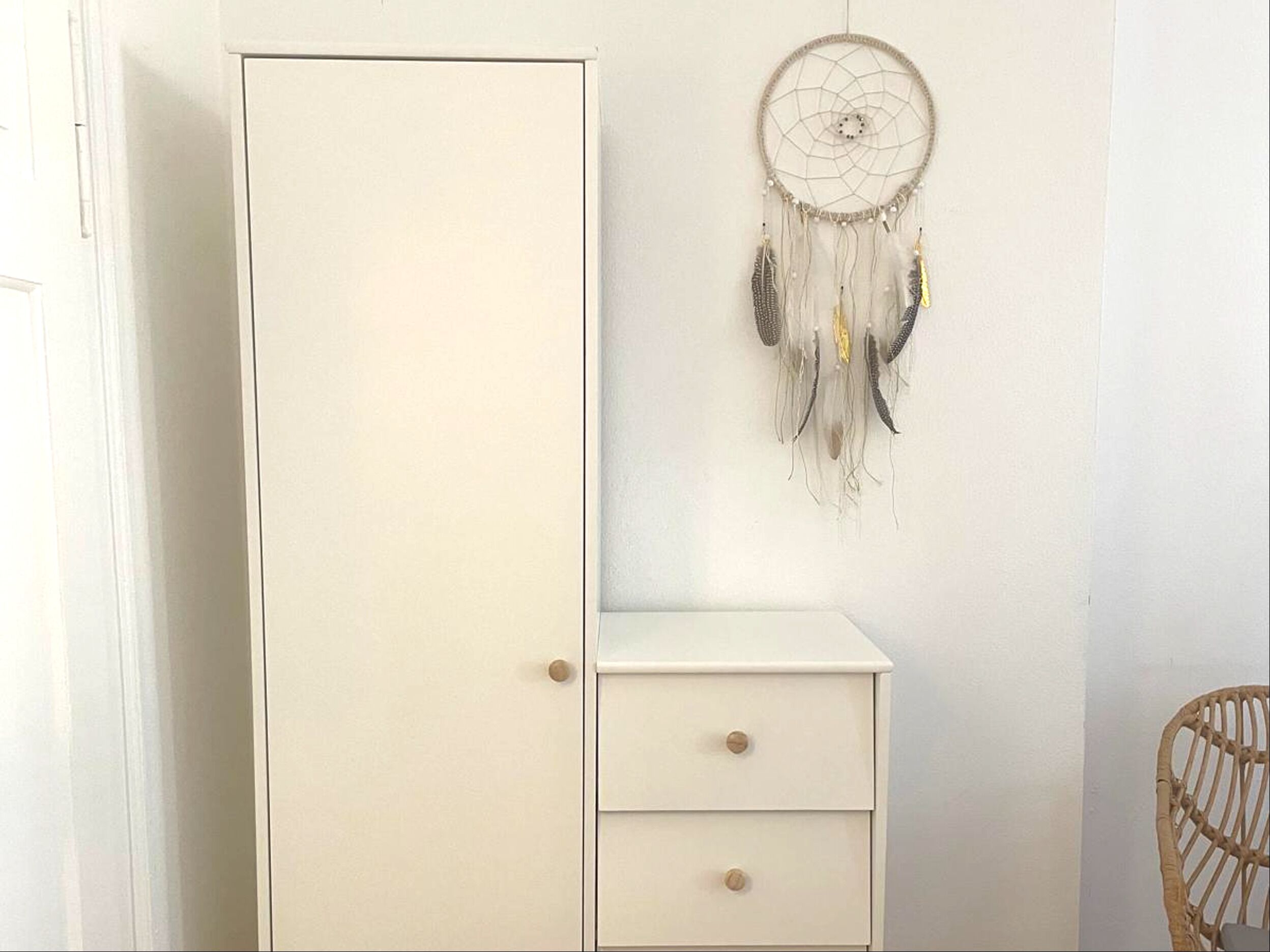 A white wardrobe with two drawers and a dreamcatcher hanging on the wall.