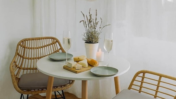 A dining area with a round table, two wicker chairs, a potted plant, and two glasses of wine. - Central | Cozy | Digitaler Check-in (Hof)