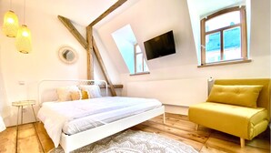 A bedroom with a bed, a yellow armchair, a TV, and a window with a view. - Central | Cozy | Digitaler Check-in (Hof)