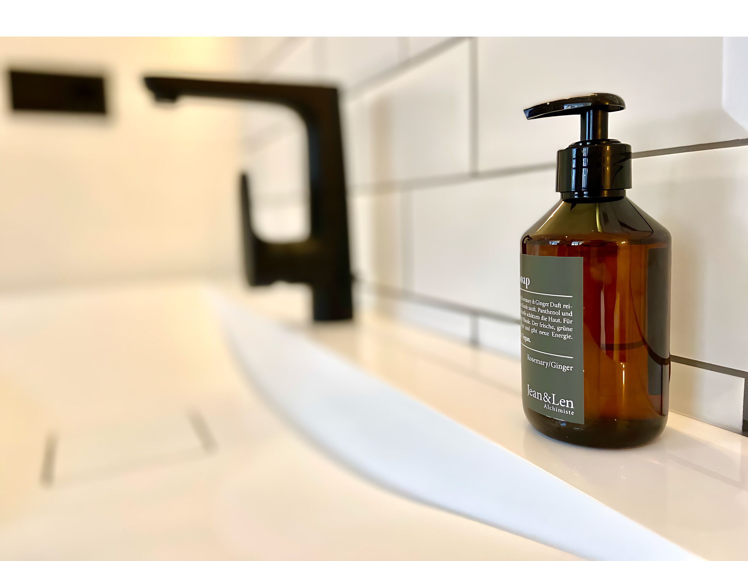 Ein Badezimmer mit einem weißen Waschbecken, einem schwarzen Wasserhahn und einer braunen Seifenflasche auf der Ablagefläche.