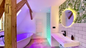 A modern bathroom with a freestanding bathtub, a white vanity with a mirror, and a wall-mounted heater. - Central | Cozy | Digitaler Check-in (Hof)