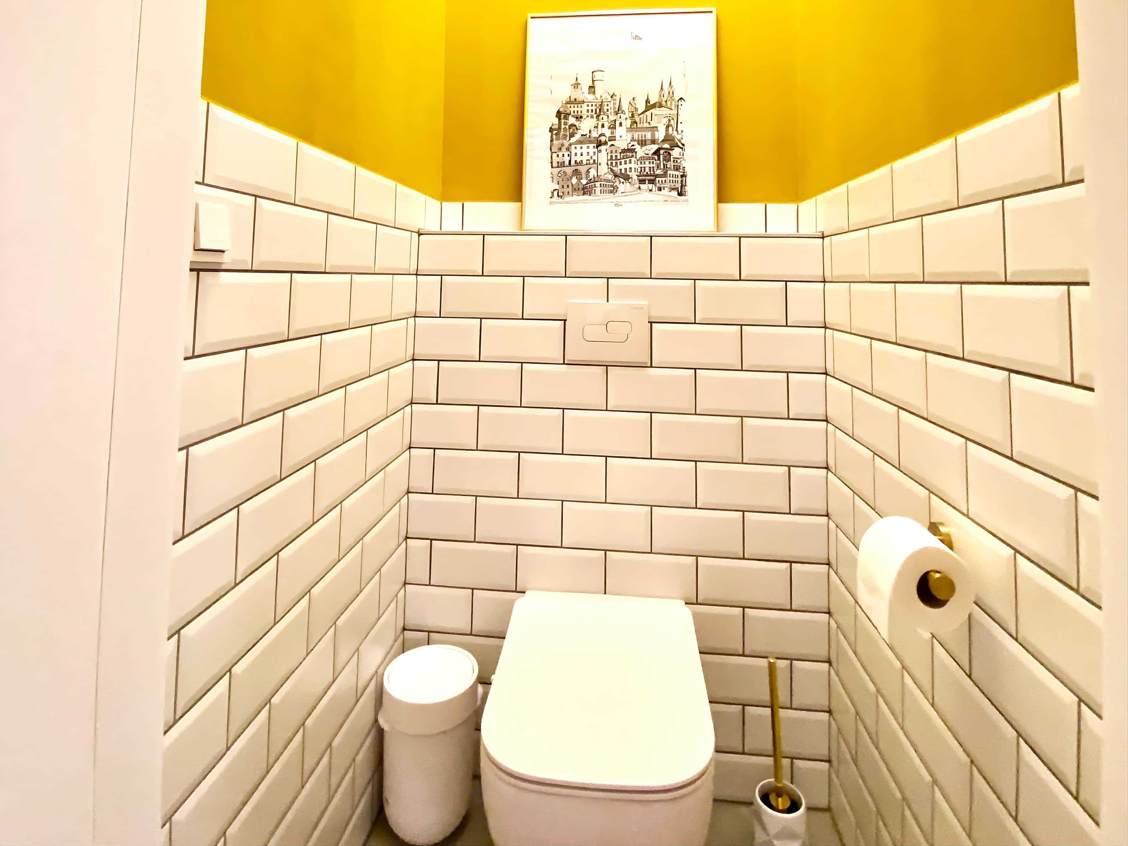 Ein kleines, modernes Badezimmer mit weißen Fliesen im U-Bahn-Stil, Toilette, Mülleimer und Toilettenbürste.