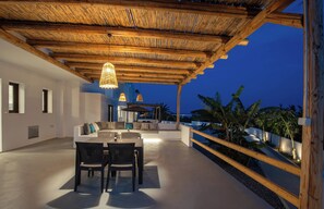 Una terrazza esterna con tetto in legno, un tavolo da pranzo con sedie e una zona relax con cuscini.