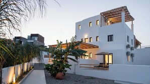 Un bâtiment moderne à la façade blanche, doté d’un espace extérieur couvert avec des sièges et d’un chemin en gravier.