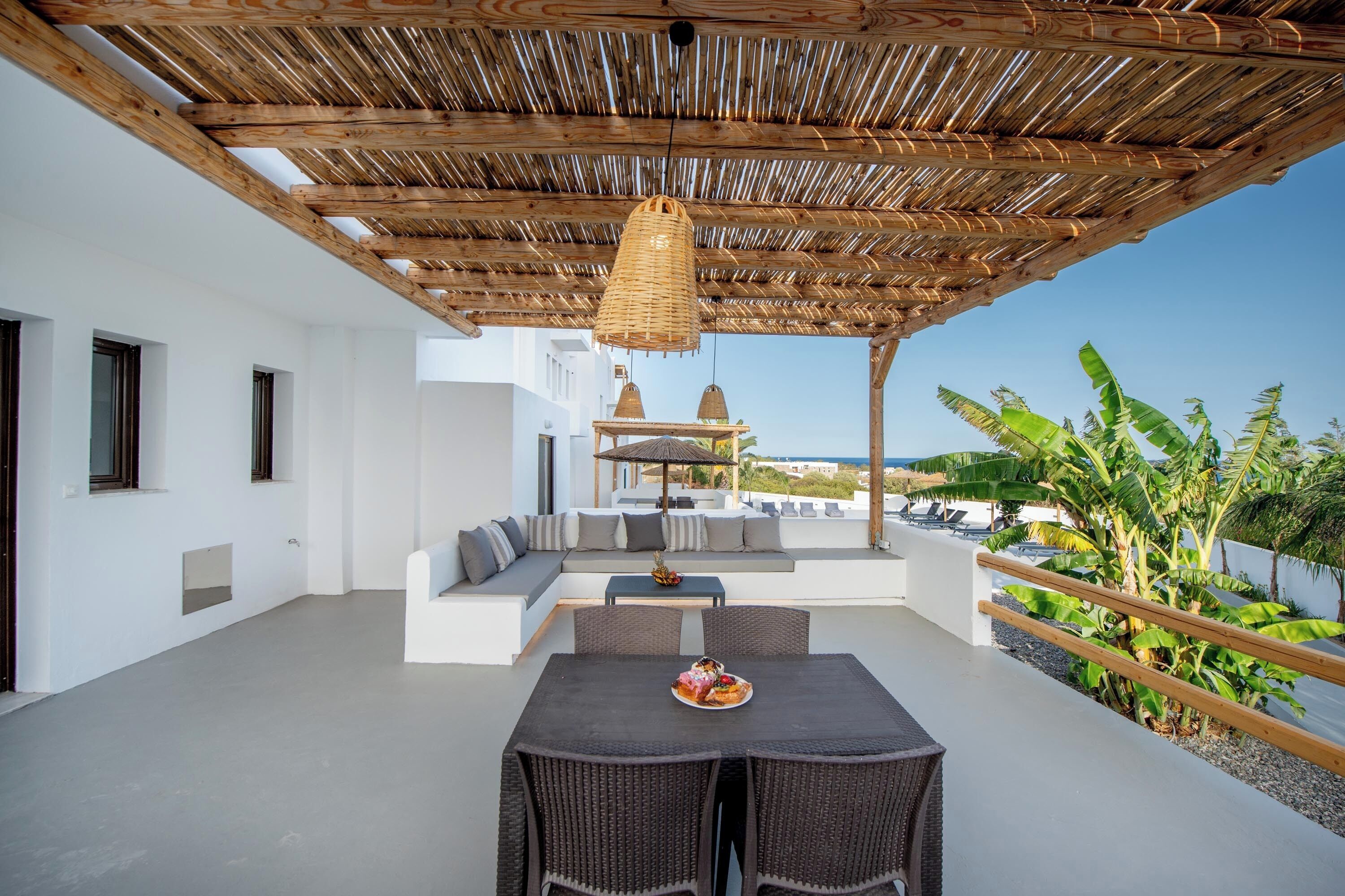 A rooftop terrace with a thatched roof, outdoor seating, a dining table with chairs, and a view of the sea.