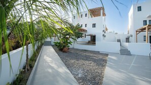 Un bâtiment moderne aux murs blancs, doté d’un chemin en béton et d’un espace recouvert de gravier où sont plantées des plantes.