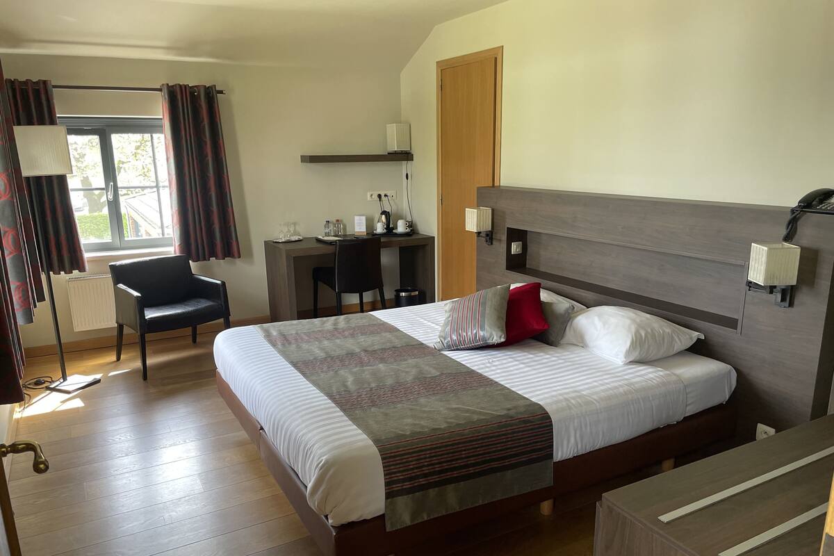 A hotel room with a large bed, a desk, a chair, and a window with curtains.