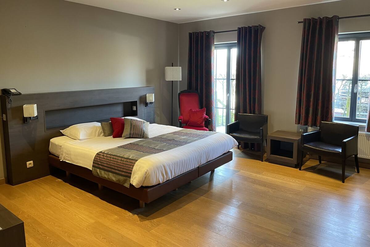 A hotel room with a large bed, a desk, a chair, and a window with curtains.