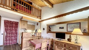 A cozy kitchen with wooden cabinets, a dining table, and a balcony with a wooden railing. - Mezzanine studio in Combloux center with parking (Combloux)
