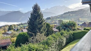 A mountainous landscape with a prominent evergreen tree in the foreground, houses with sloped roofs, and a view of distant mountains. - Mezzanine studio in Combloux center with parking (Combloux)