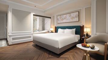Habitación de hotel con una cama grande, una zona de estar con una silla, una pequeña mesa con fruta y un baño con bañera y espejo.