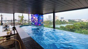 Una piscina infinita con vistas a la ciudad, mobiliario exterior y un mural.