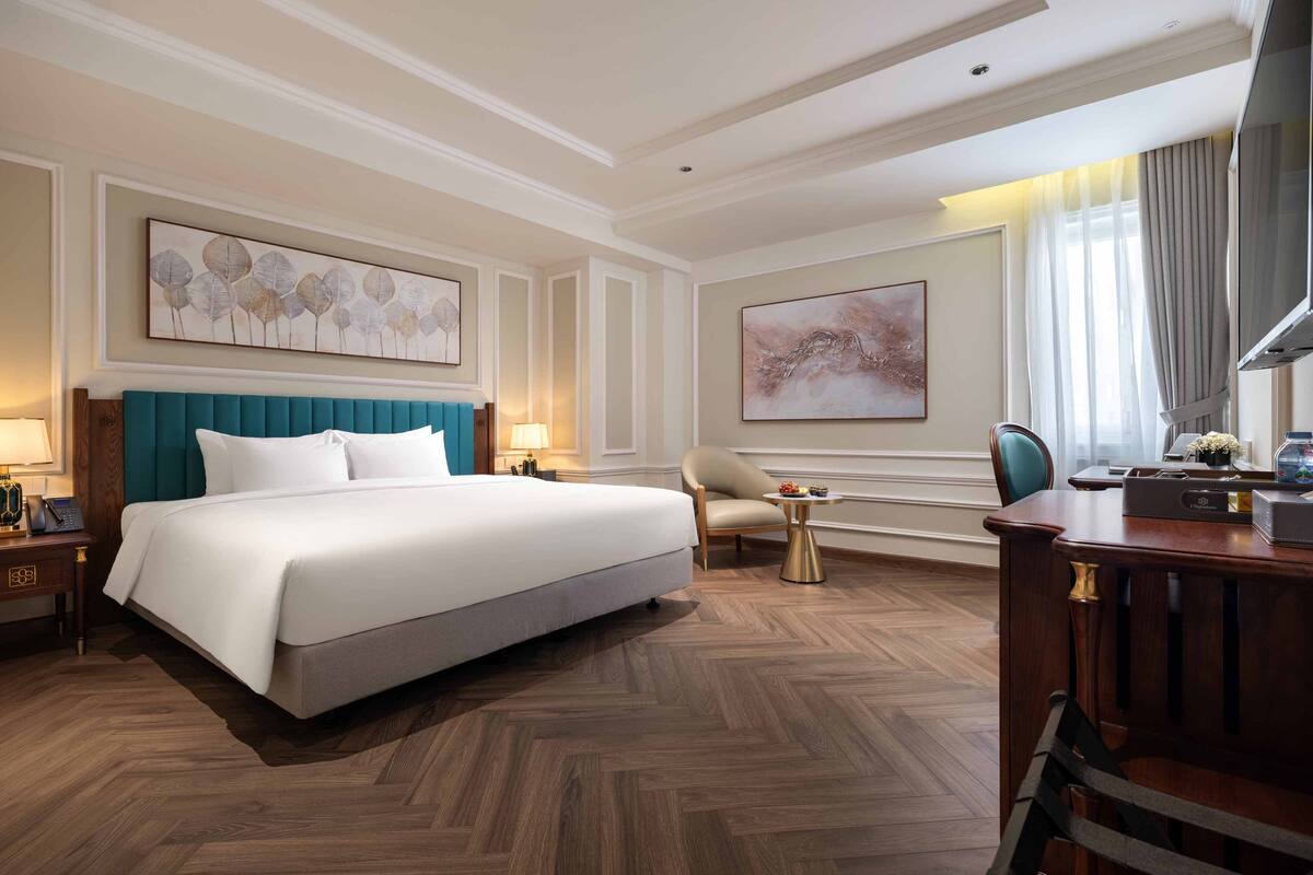 A hotel room with a large bed, a desk, a chair, and artwork on the walls.