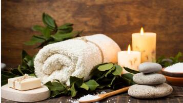 A spa setting with a rolled towel, candles, stones, and a soap bar.